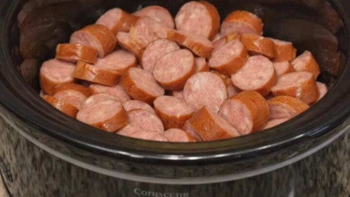 Close up of glazed smoked sausage and pineapple chunks in a black slow cooker