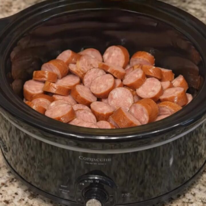 Close up of glazed smoked sausage and pineapple chunks in a black slow cooker