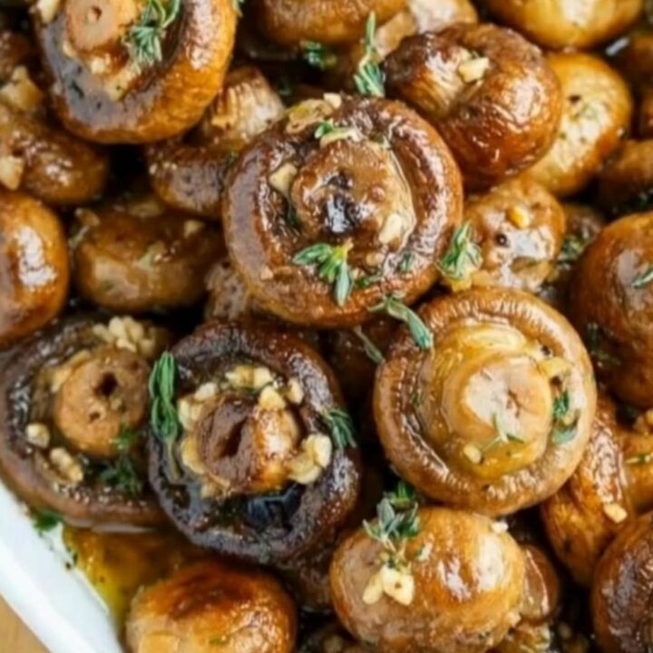 A white oval serving dish filled with golden-brown sautéed mushrooms glistening in a rich garlic butter sauce.