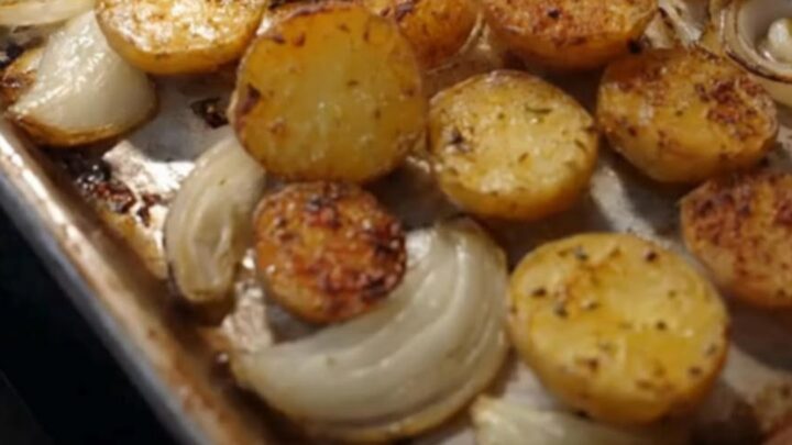 A golden, crispy roasted potato and onion dish served on a white plate with fresh herbs sprinkled on top.