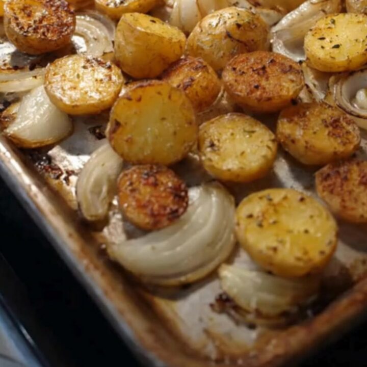 A golden, crispy roasted potato and onion dish served on a white plate with fresh herbs sprinkled on top.