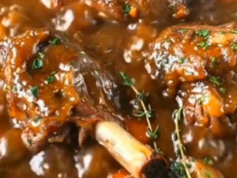 A rustic Dutch oven filled with tender, slow-braised lamb shanks, carrots, and baby potatoes in a rich brown gravy.