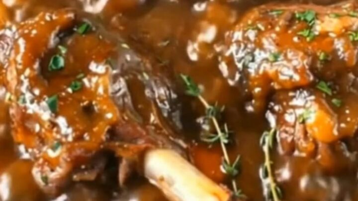 A rustic Dutch oven filled with tender, slow-braised lamb shanks, carrots, and baby potatoes in a rich brown gravy.