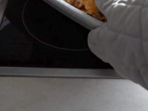 A bubbly, golden-brown lasagna roll being lifted from a white baking dish with a spatula
