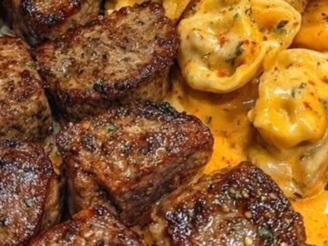 A close-up of garlic butter steak bites and cheesy tortellini on a white plate.