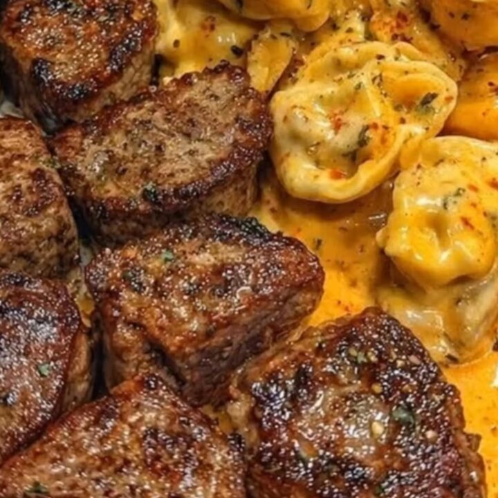 A close-up of garlic butter steak bites and cheesy tortellini on a white plate.