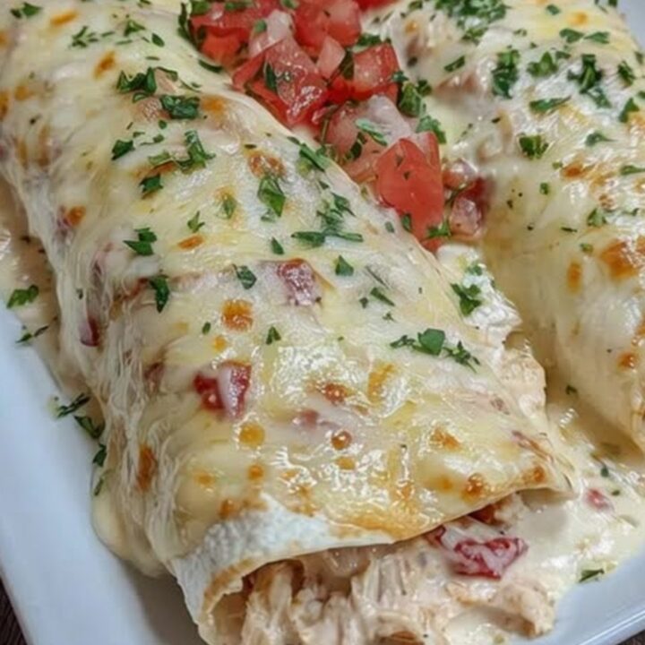 A white platter filled with golden-brown, cheesy queso chicken enchiladas garnished with diced tomatoes and fresh herbs.