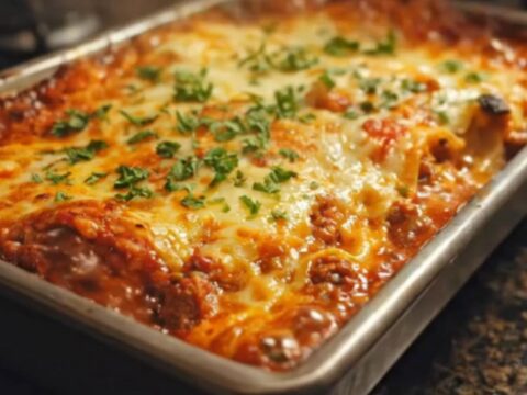 A golden-brown lasagna in a metal baking pan with melted cheese and fresh parsley.