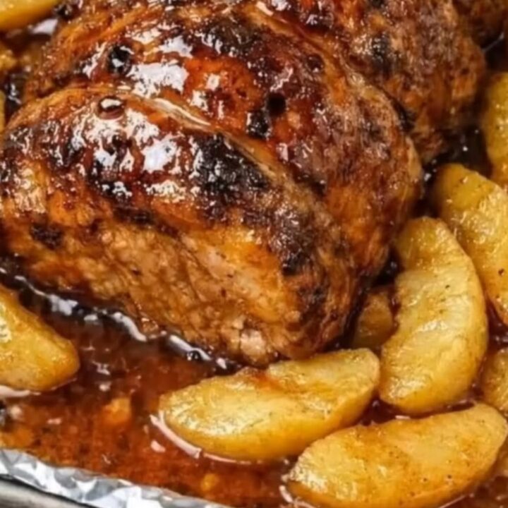 A beautifully roasted honey garlic pork loin surrounded by caramelized apple slices on a white platter.