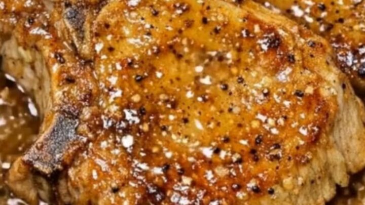 A close-up of a succulent, bone-in pork chop coated in a dark, glossy honey garlic glaze on a white plate.