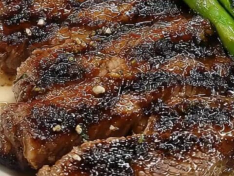A platter featuring a perfectly seared medium-rare steak sliced into strips next to charred asparagus.