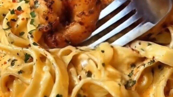 A steaming portion of fettuccine coated in creamy Cajun Alfredo sauce topped with blackened shrimp in a shallow bowl.