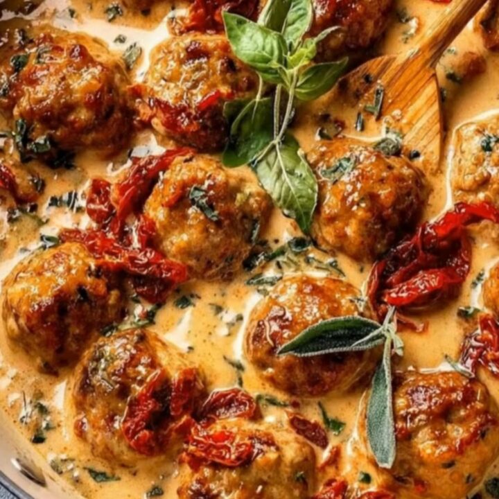 Golden brown chicken meatballs in a creamy sun-dried tomato sauce with steam rising from the skillet.