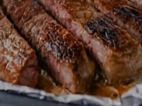 A close-up of seared steak slices and golden roasted potatoes on a foil-lined baking sheet.