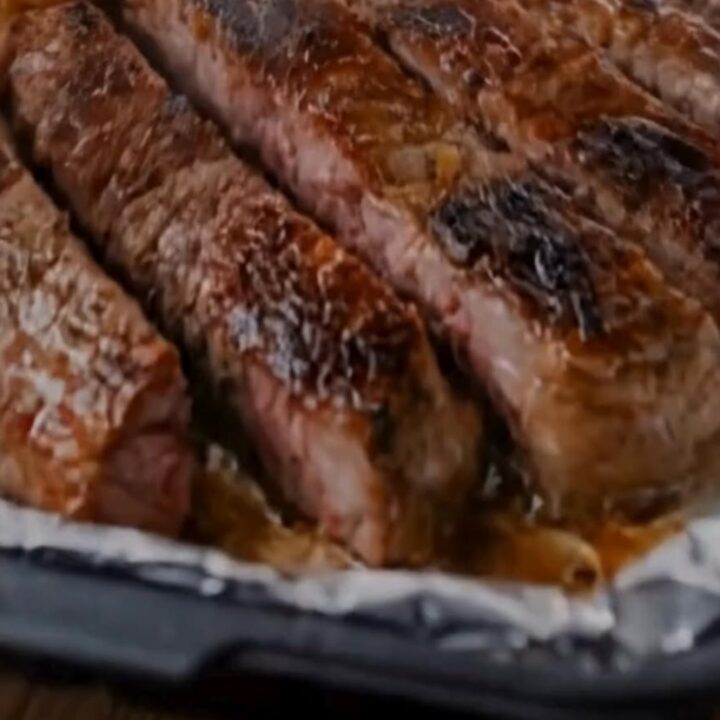 A close-up of seared steak slices and golden roasted potatoes on a foil-lined baking sheet.