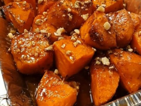 A close-up of caramelized brown sugar glazed sweet potato chunks topped with chopped nuts in a pan.