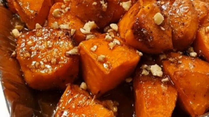 A close-up of caramelized brown sugar glazed sweet potato chunks topped with chopped nuts in a pan.