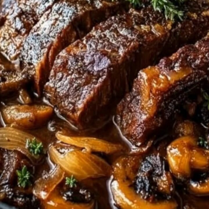 A close-up of a tender slice of beef chuck roast covered in a rich, dark mushroom and caramelized onion gravy.