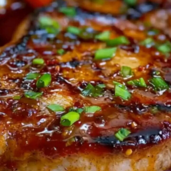 A close-up of a perfectly seared pork chop topped with caramelized peach slices and a glossy glaze.