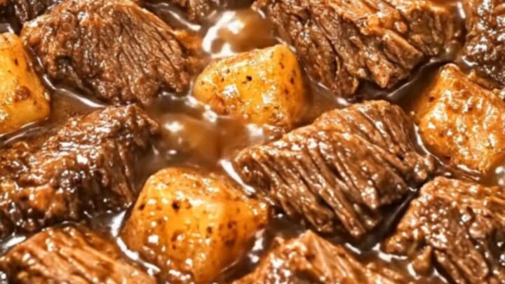 A steaming bowl of slow-cooked beef stew with chunky potatoes in a rich brown gravy.