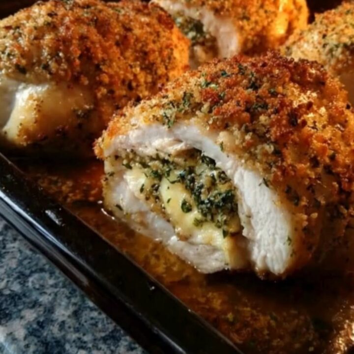 A golden, crispy oven-baked stuffed chicken breast resting in a glass dish with melted cheese oozing out.