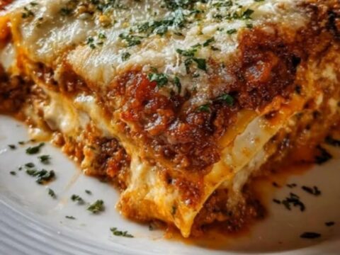 A steaming square of cheesy meat lasagna served in a glass baking dish.