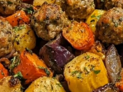 A close-up of a baking dish filled with roasted beef meatballs, bell peppers, red onions, and golden potatoes.