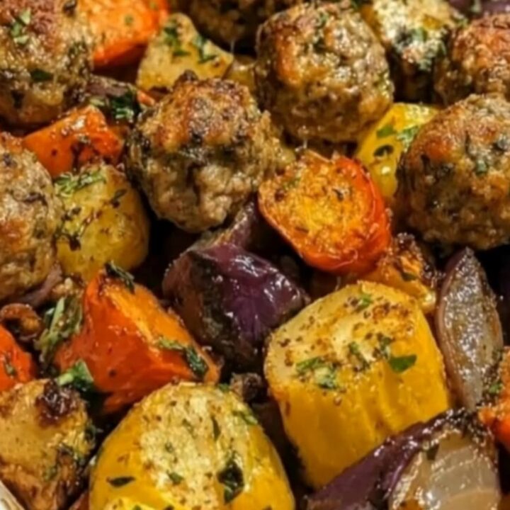 A close-up of a baking dish filled with roasted beef meatballs, bell peppers, red onions, and golden potatoes.