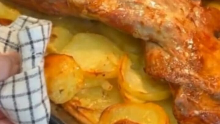 A golden-brown slow-roasted lamb shoulder resting on a bed of sliced potatoes in a roasting pan.