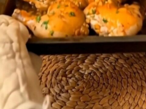 A golden-brown crispy chicken thigh resting in a baking pan with rich garlic butter juices.