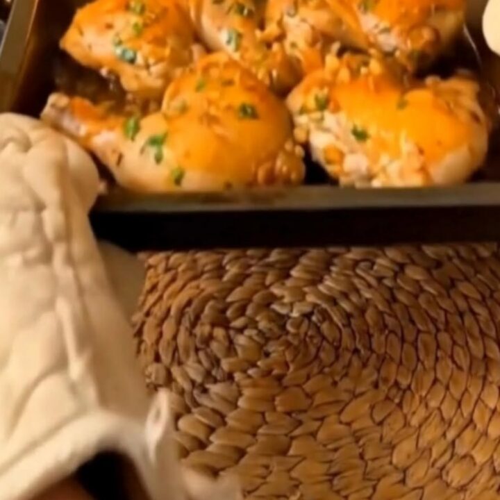 A golden-brown crispy chicken thigh resting in a baking pan with rich garlic butter juices.