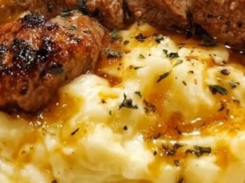 A plate of garlic butter steak bites sitting on a bed of creamy mashed potatoes with steam rising.