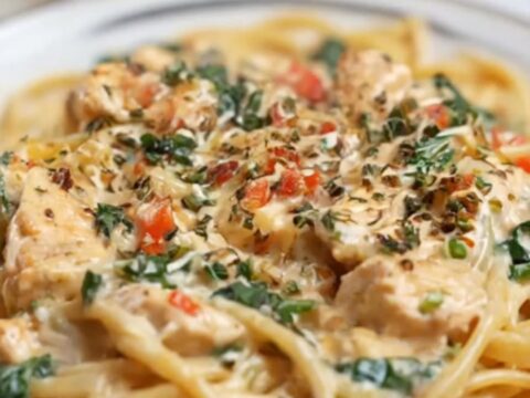 A steaming bowl of creamy garlic parmesan chicken linguine with fresh spinach and herbs.