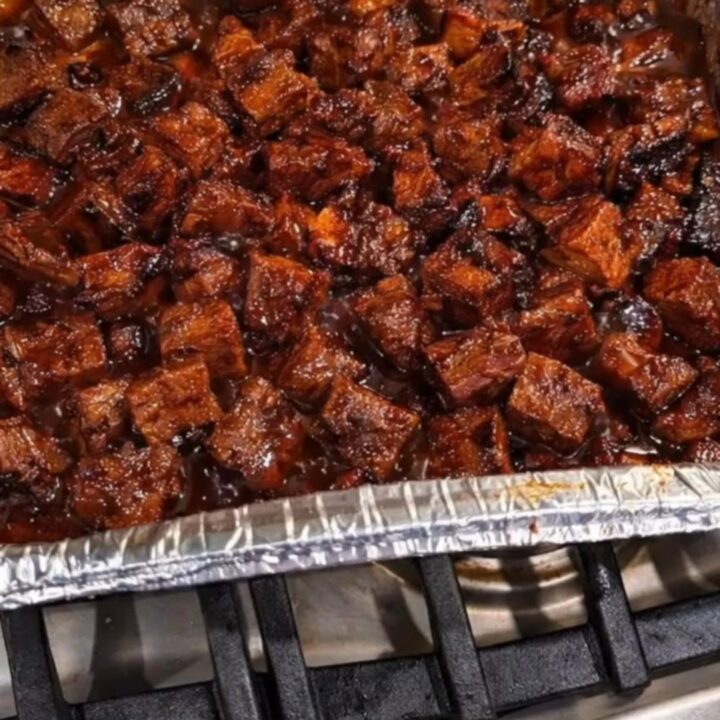 Glossy, caramelized beef burnt ends in an aluminum foil pan, steaming and ready to serve.