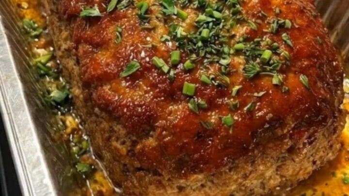 A thick, juicy slice of sweet glazed meatloaf resting on a white plate with fresh green herbs.
