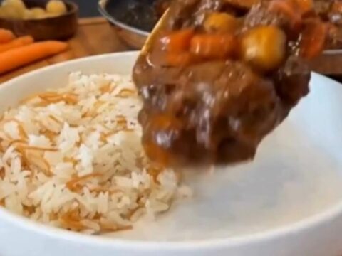 A steaming bowl of beef stew featuring tender chunks of beef, carrots, and potatoes served next to white vermicelli rice.