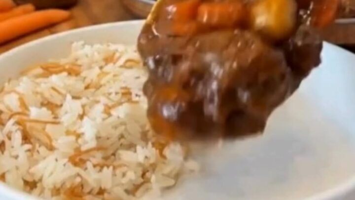 A steaming bowl of beef stew featuring tender chunks of beef, carrots, and potatoes served next to white vermicelli rice.