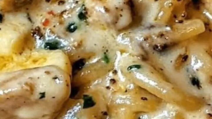 A close-up of creamy chicken spaghetti with fresh spinach on a plain white plate.