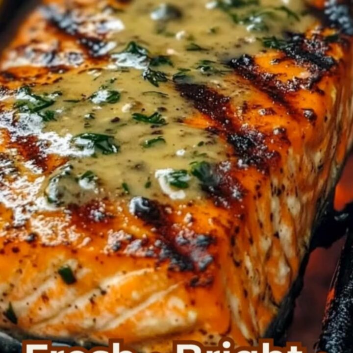 A close-up of a perfectly grilled salmon fillet with visible sear marks, topped with a melting herb butter on a wooden board.