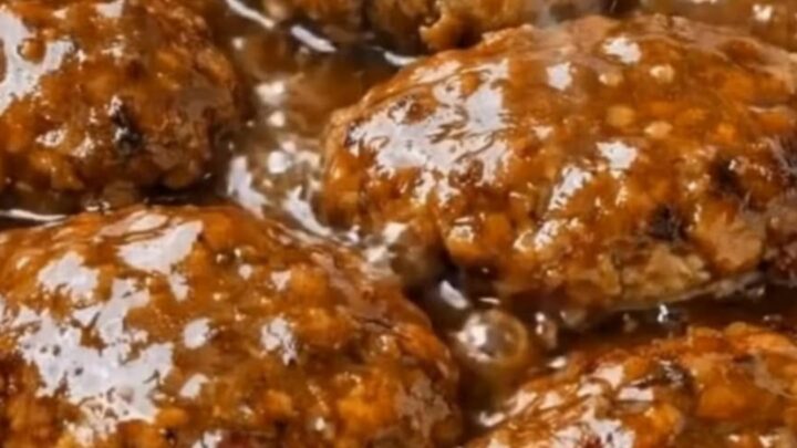 A close-up of a tender Salisbury steak patty covered in rich onion gravy on a plate.