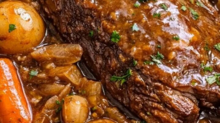 A close-up of a tender, fall-apart pot roast resting in a rich brown gravy with carrots and baby potatoes.