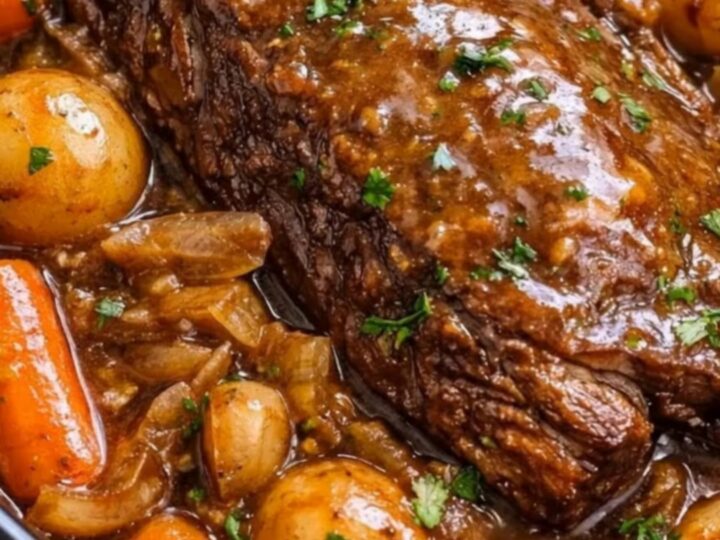 A close-up of a tender, fall-apart pot roast resting in a rich brown gravy with carrots and baby potatoes.