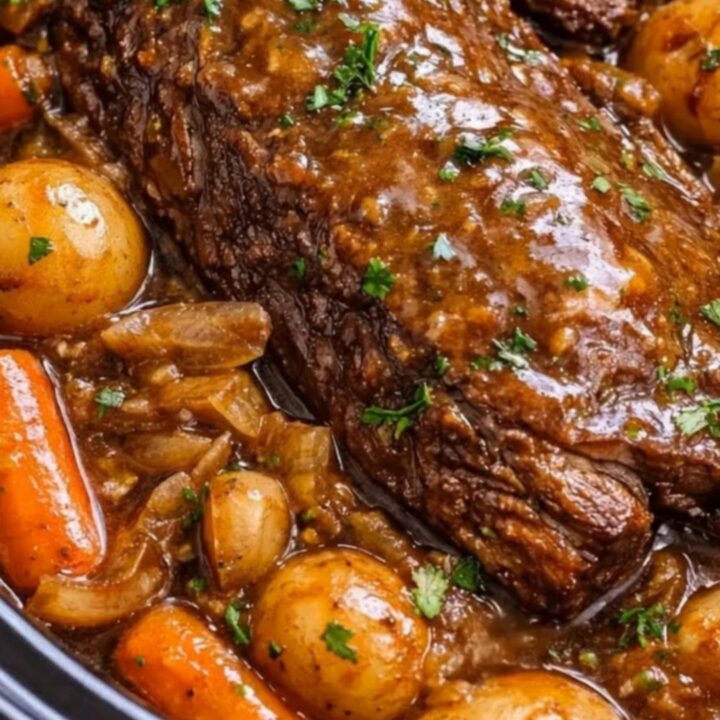 A close-up of a tender, fall-apart pot roast resting in a rich brown gravy with carrots and baby potatoes.