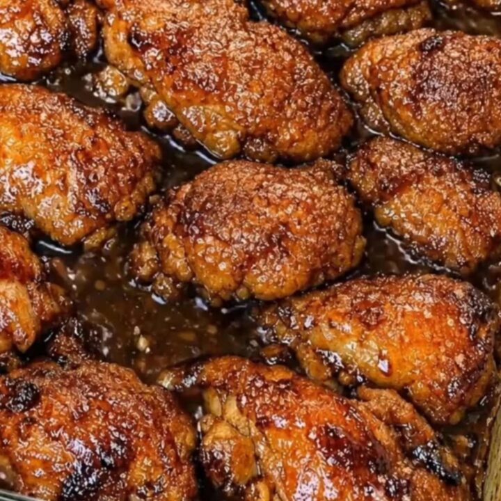 Close up of sticky honey garlic chicken thighs with a glossy glaze in a baking dish.