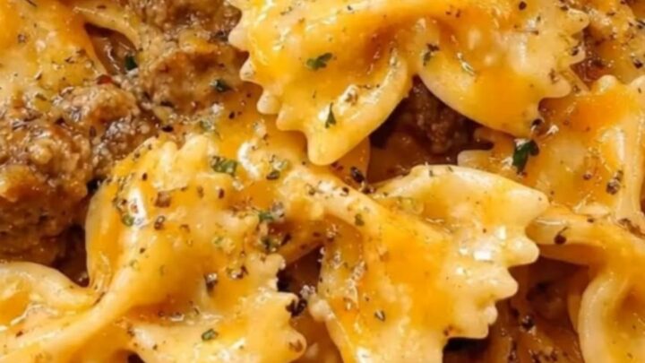 A large white dish filled with creamy bowtie pasta, browned ground beef, melted cheddar cheese, and fresh parsley.
