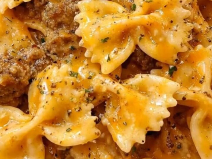 A large white dish filled with creamy bowtie pasta, browned ground beef, melted cheddar cheese, and fresh parsley.