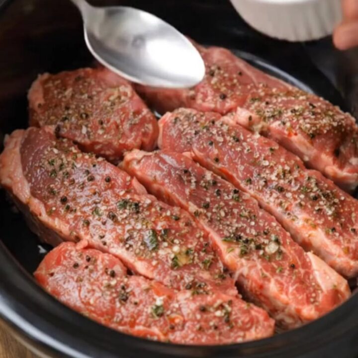 Tender, glistening slow-cooked steak strips served on a white plate with garlic butter sauce.