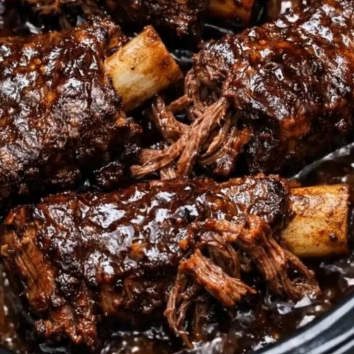 A close-up of tender Guinness beef short ribs served in a dark, glossy gravy on a white plate.