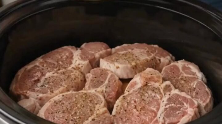 A juicy pork chop topped with tender cinnamon-spiced apples resting in a black slow cooker insert.
