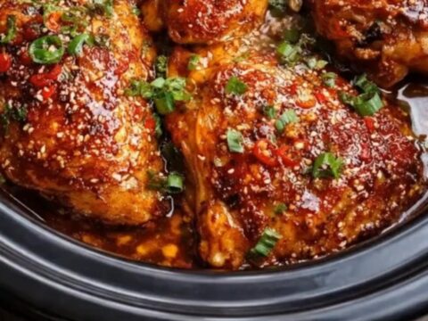 A close-up of sticky honey garlic chili chicken thighs garnished with sesame seeds and scallions.